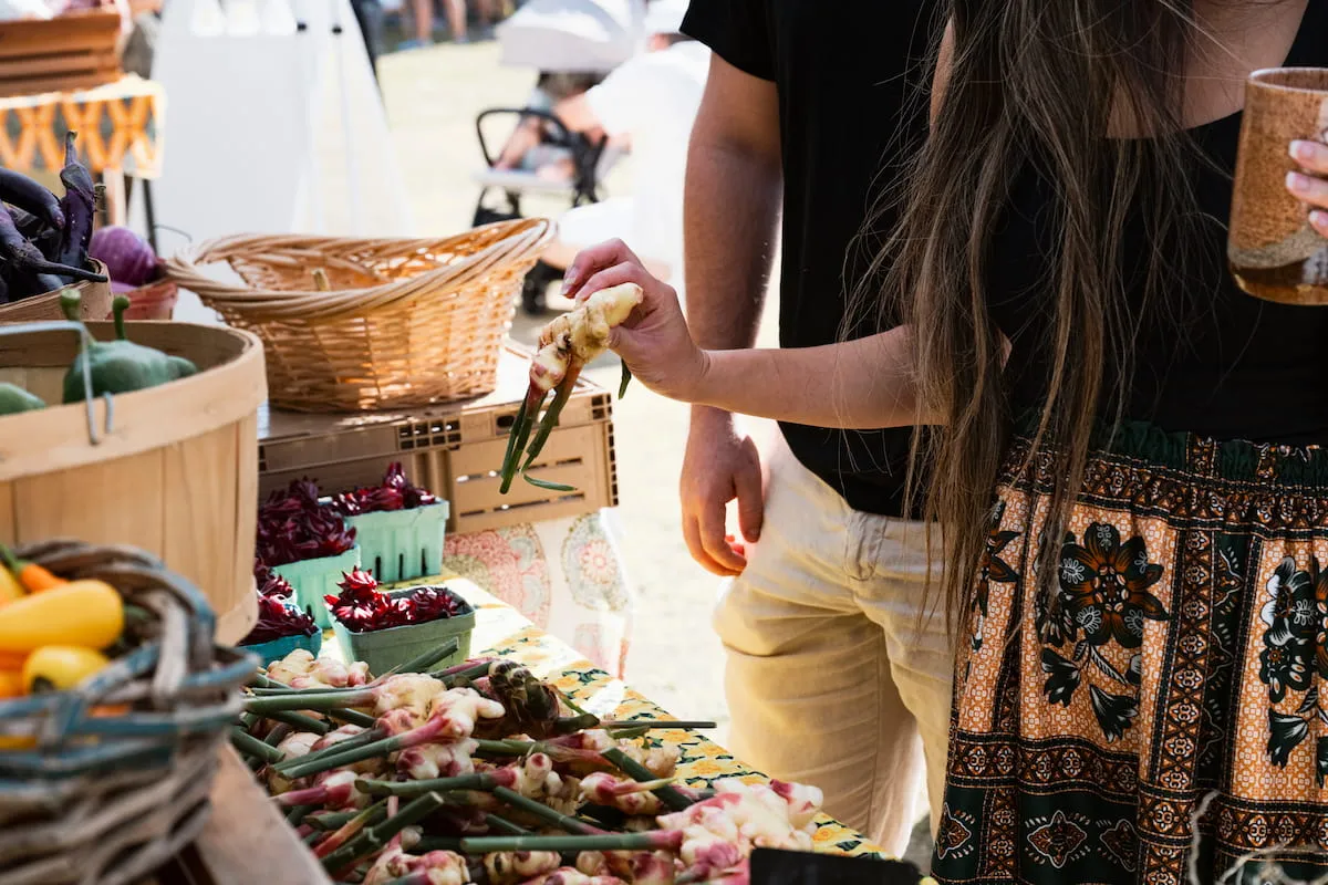 A couple inspects ginger root and other vegetables at a farmers booth.