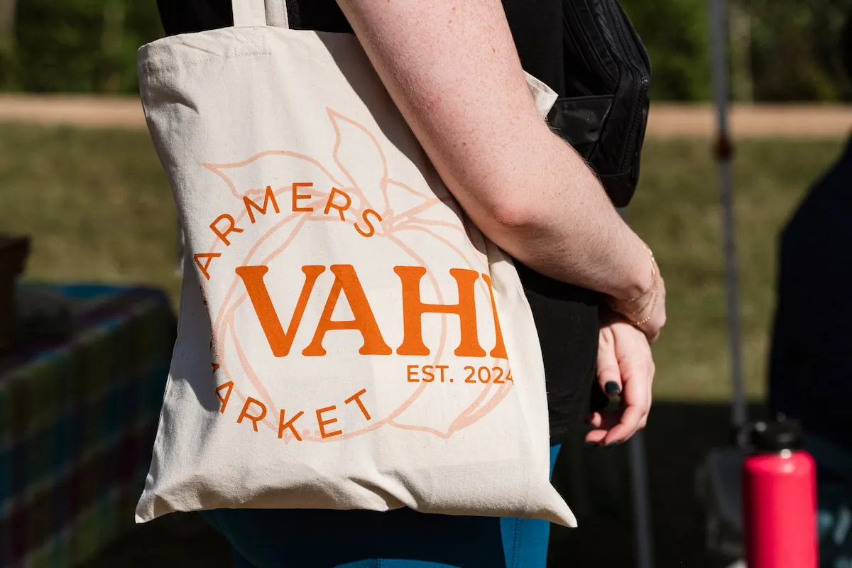 A woman stands in line carrying her VaHi Farmers Market tote bag.