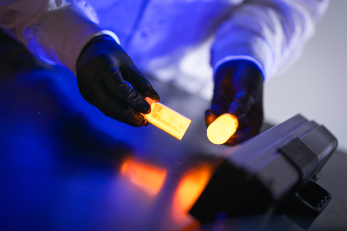 Gloved hands holding jars of glowing quantum dots.