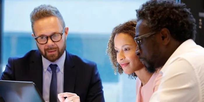 Three people, two appearing to be investors and one advisor, are looking at a laptop screen during a meeting.