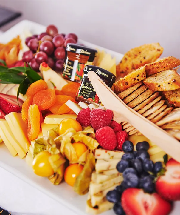Platter with grapes, cheese, dried apricots, crackers, berries, and small jam jars.
