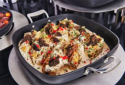 Pan with chicken breasts in creamy sauce topped with herbs and morel mushrooms.