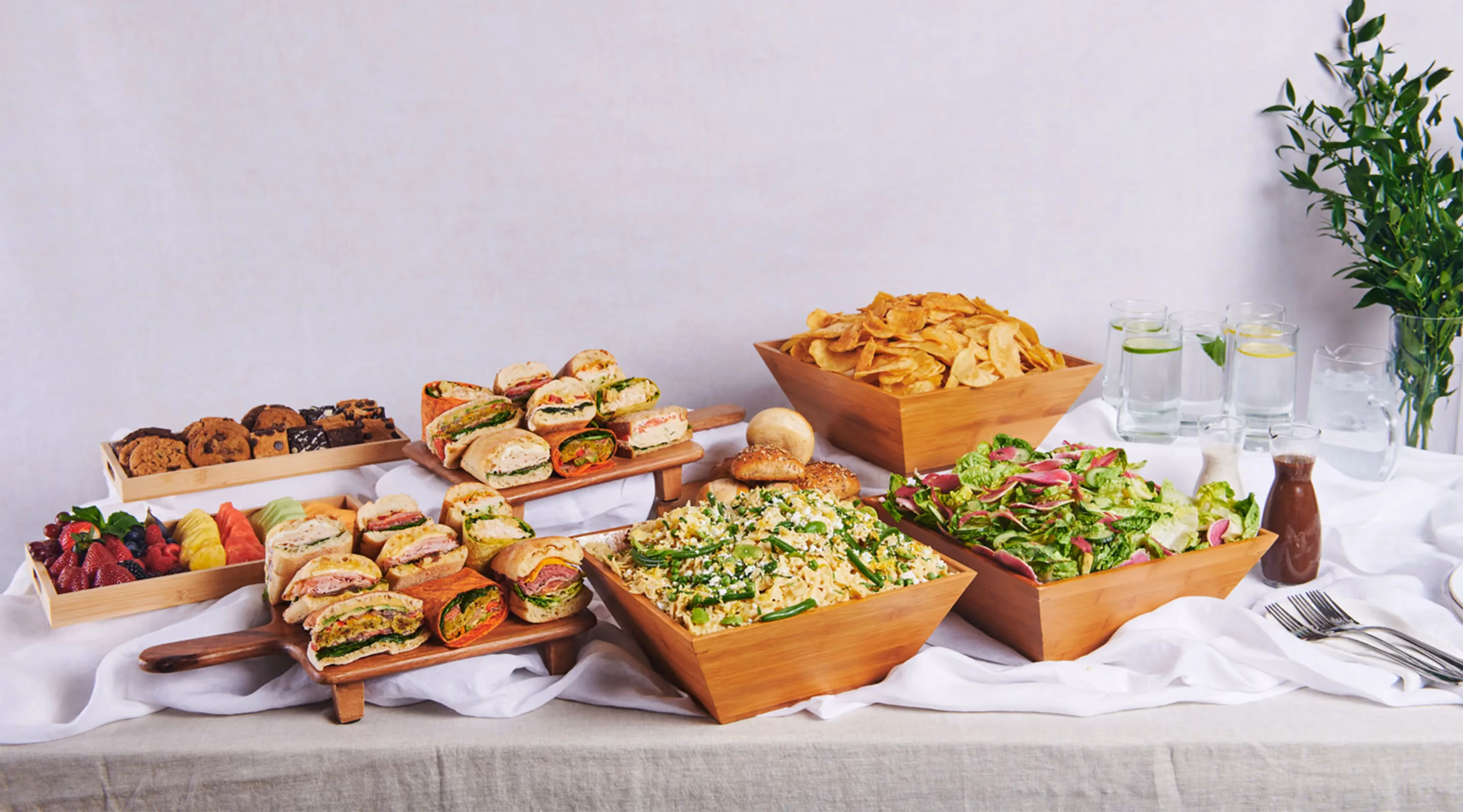 Workplace catering buffet with sandwiches, salad, pasta, chips, fruit, cookies, and flavored water.