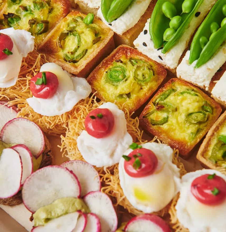 Close-up of assorted gourmet appetizers with vegetables, cream, and garnishes on a wooden board.