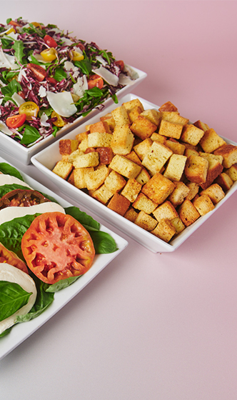 Catering spread with roasted potatoes, caprese salad, and mixed greens served on white trays.