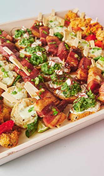 Chicken, mozzarella, and tomato skewers with pesto, parmesan, and fresh herbs served on a catering platter.