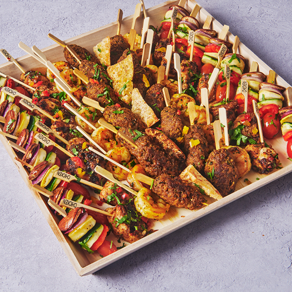 Mediterranean skewer platter with grilled chicken, beef, vegetables, and pita served in a wooden catering tray.