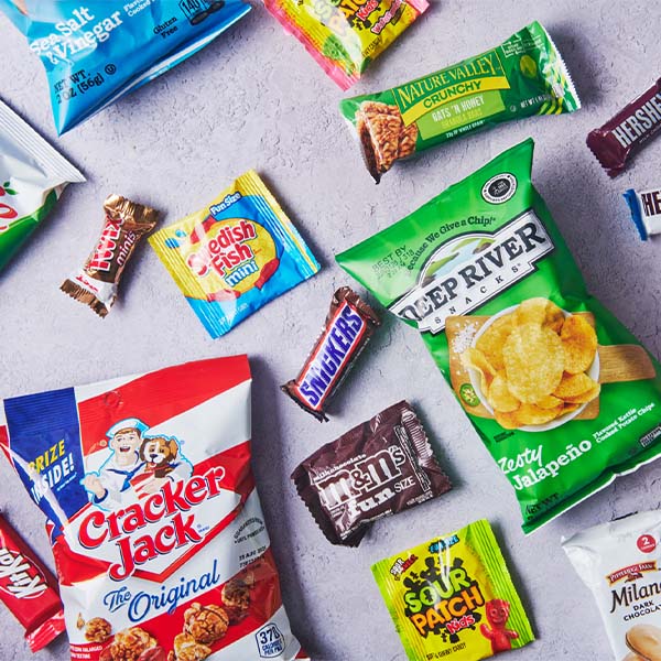 Assorted packaged snacks, chips, candy, and Cracker Jack arranged on a light gray surface.