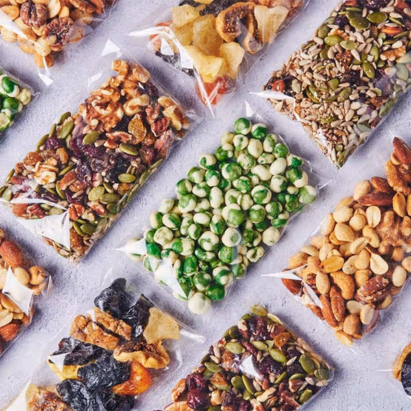 Assorted snack packs, trail mix, nuts, and candy displayed in clear bags.