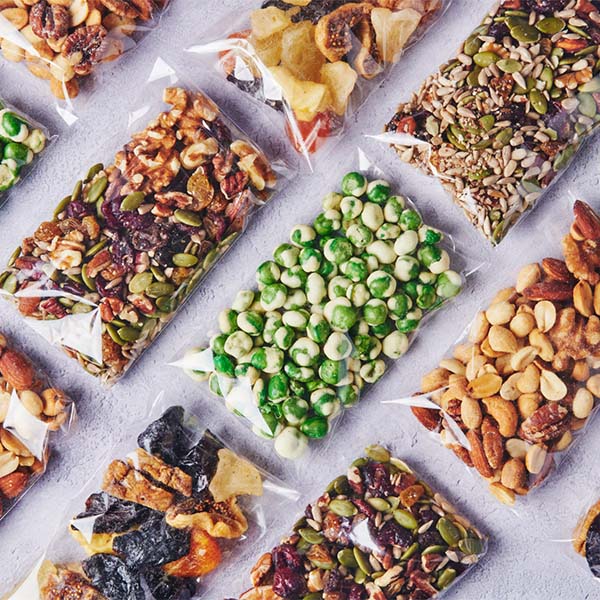 Assorted snack packs, trail mix, nuts, and candy displayed in clear bags.