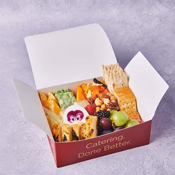 Branded catering snack box filled with cheese, crackers, fruit, vegetables, and dips.