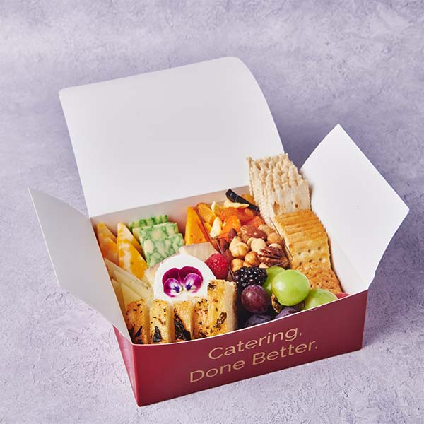 Branded catering snack box filled with cheese, crackers, fruit, vegetables, and dips.