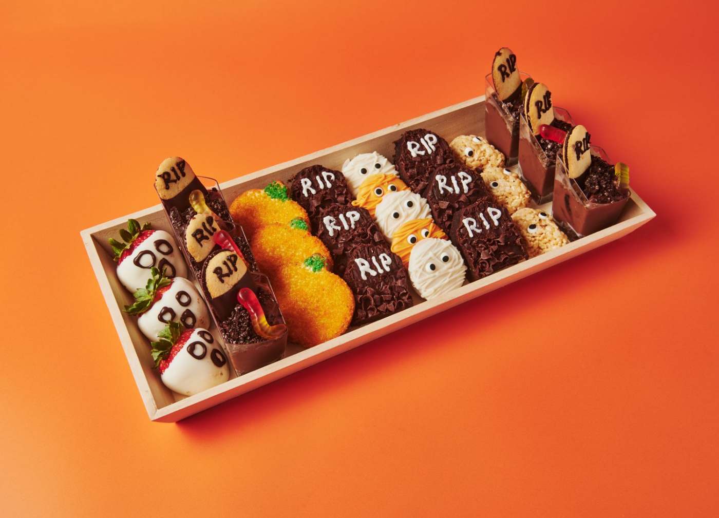 Spooky sweets display with RIP brownies, mummy cookies, pumpkin cakes, ghost strawberries and mousse shooters (VEG)