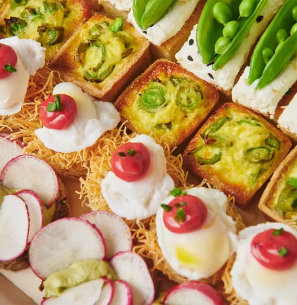 Close-up of assorted gourmet appetizers with vegetables, cream, and garnishes on a wooden board.