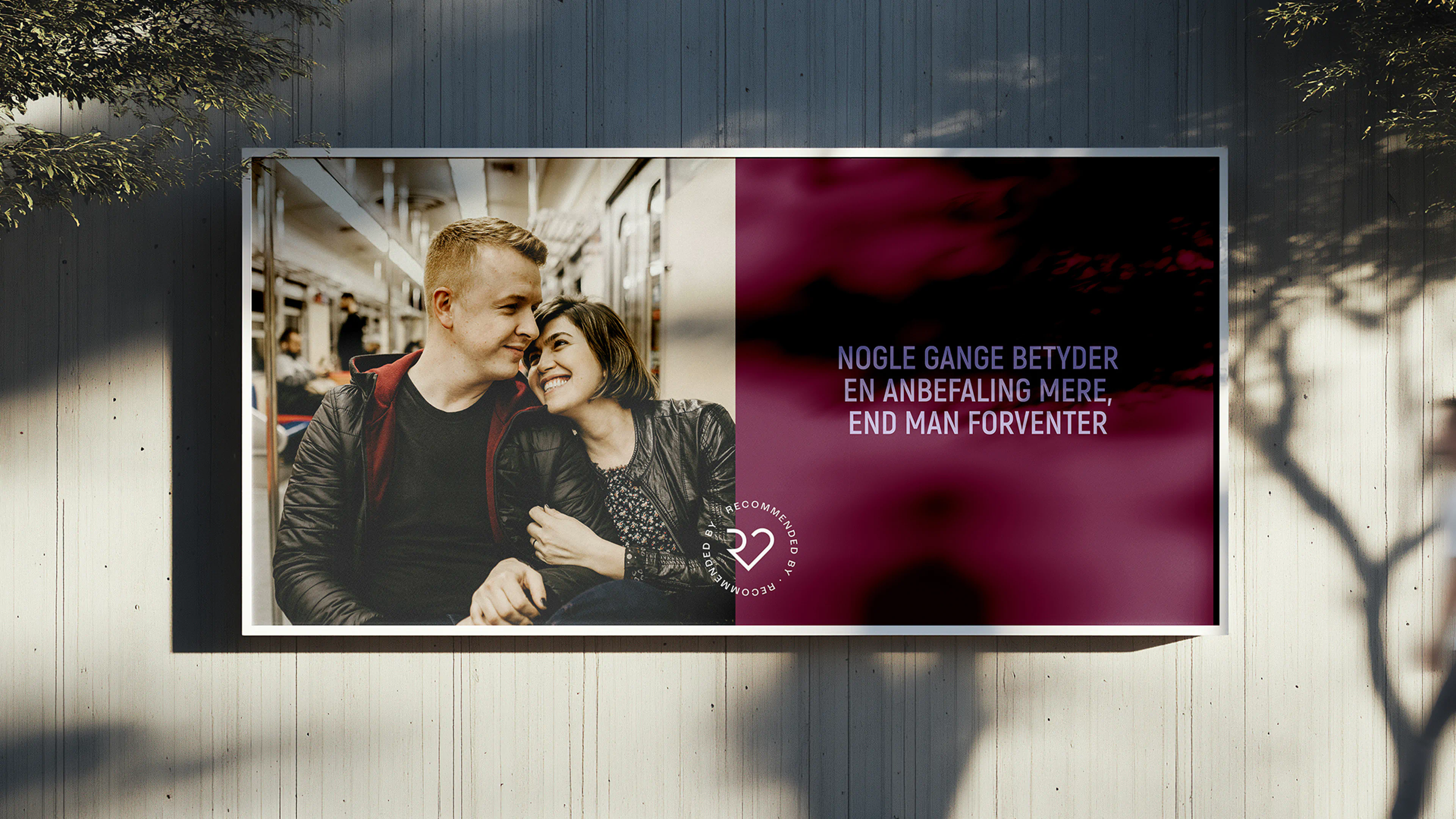 Billboard ad with a smiling couple on public transport and brand message in Danish, showcasing Recommendating’s commercial identity.