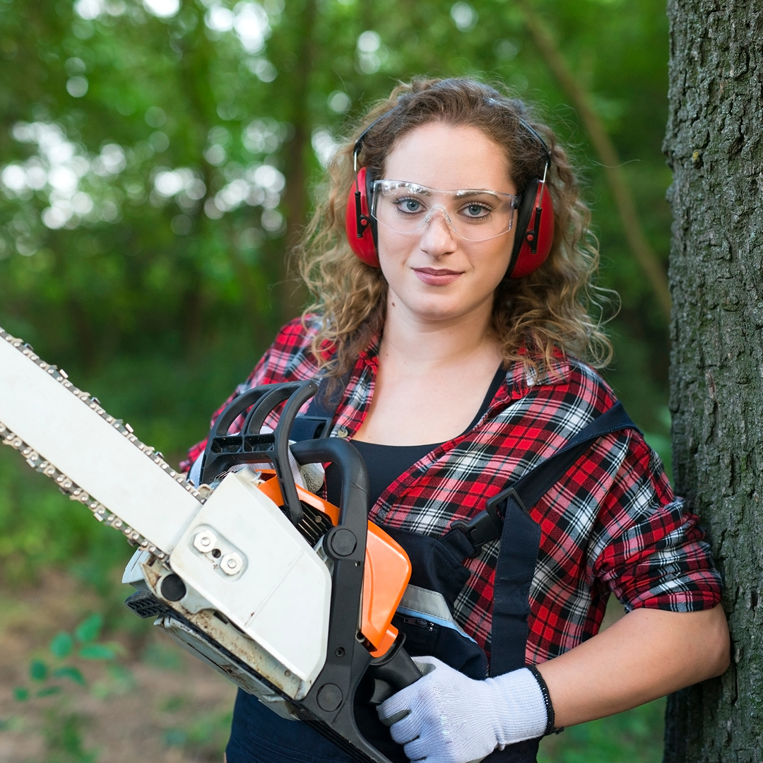 Arborist trimming a tree branch with safety harness and helmet