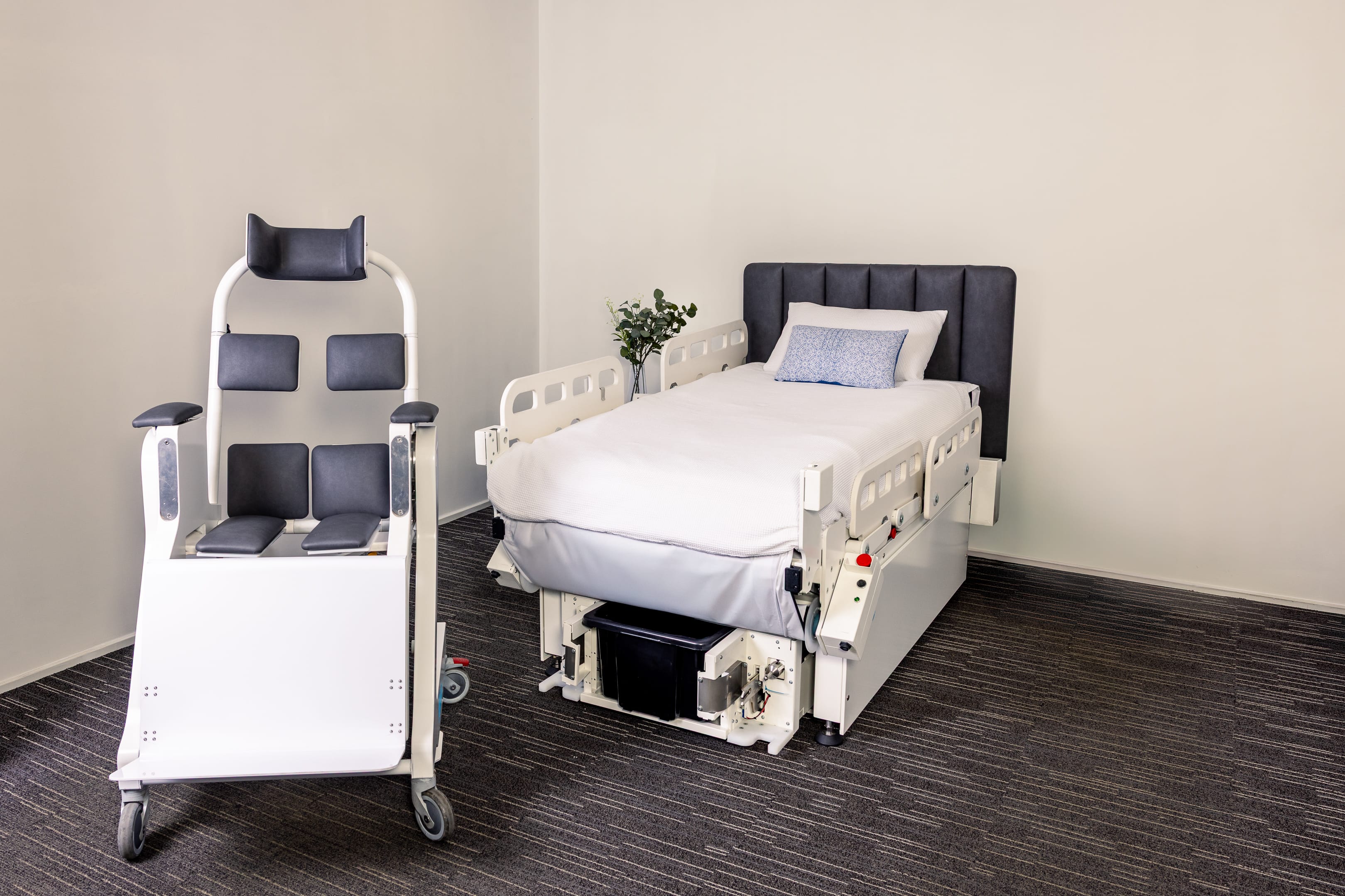 Behn® assistive chair positioned beside bed with side rails lowered and raised, showing adjustable configurations