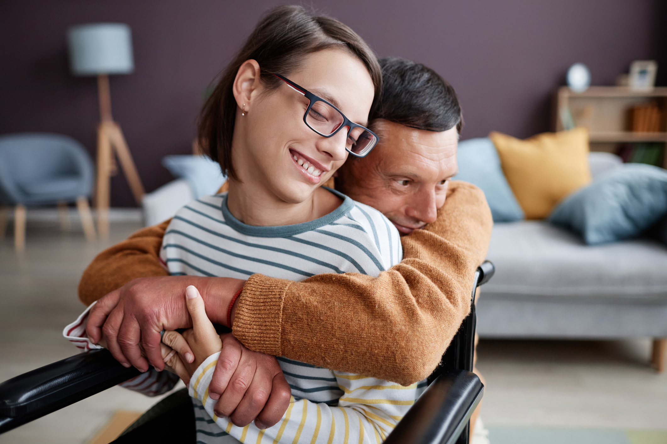 Man embracing smiling woman in wheelchair at home, showing love, support and connection in daily life