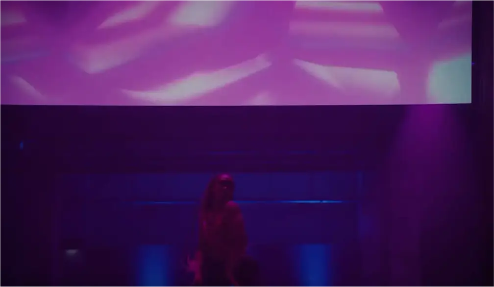 Silhouette of a person standing in a dark room with purple and blue lighting and abstract light patterns on the ceiling.