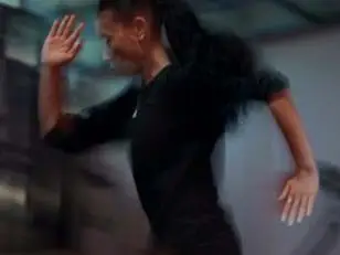 One person in motion wearing a black long-sleeve top, running indoors with a blurred background of gray and blue tones.