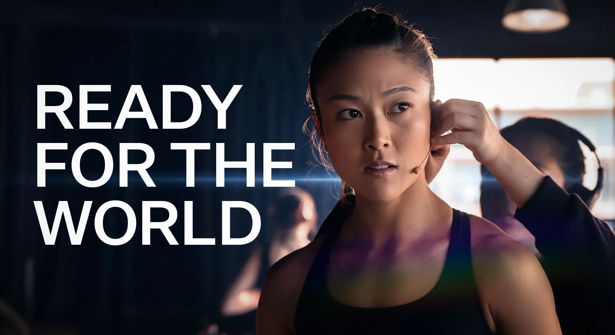 Athlete wearing a headset microphone being assisted by a technician in a dimly lit room with the text 'READY FOR THE WORLD' on the left.