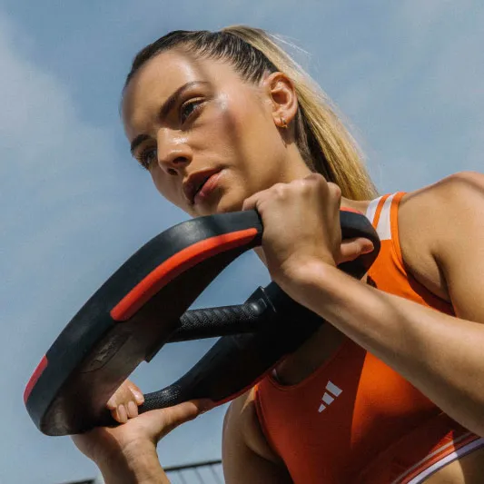 A woman in fitness wear holding a weight plate from a LES MILLS SMARTBAR