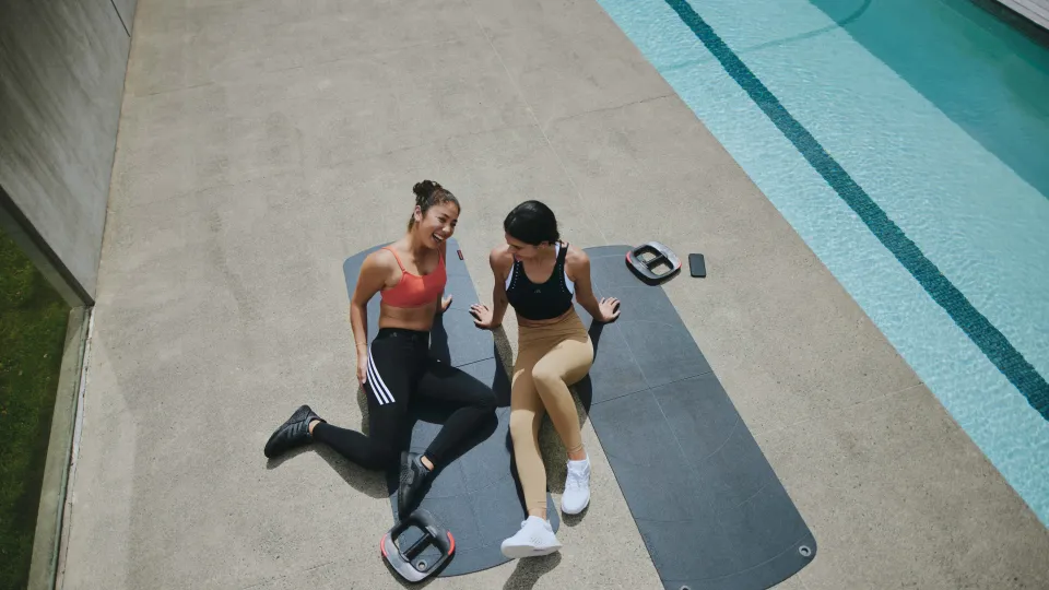 Two instructors sitting on yoga mats and laughing