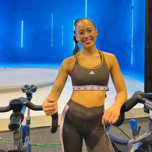 Image of Dee Rowell standing between two stationary bikes and smiling.
