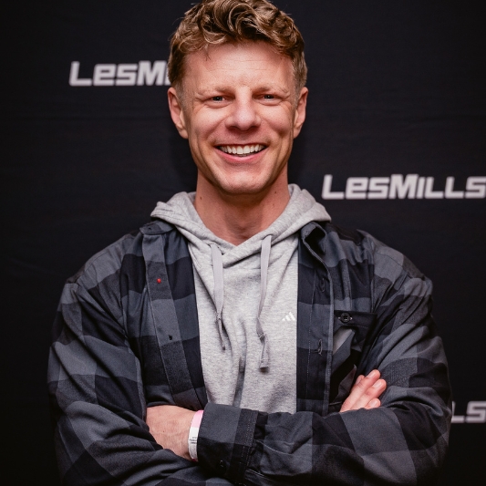 Image of Bas Hollander, smiling, wearing a grey hoodie with a plaid shirt over the top and his arms are crossed