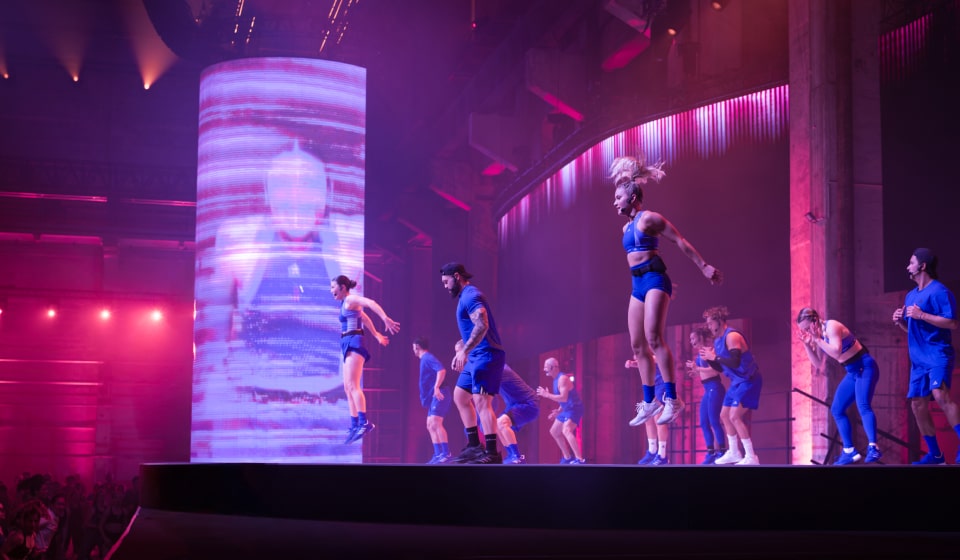 Group of Les Mills Grit instructors dressed in adidas workout gear demonstrating a workout to an audience