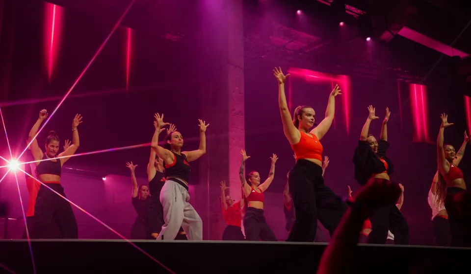 Group of Les Mills Dance instructors dressed in adidas workout gear mid way through demonstrating the workout to an audience