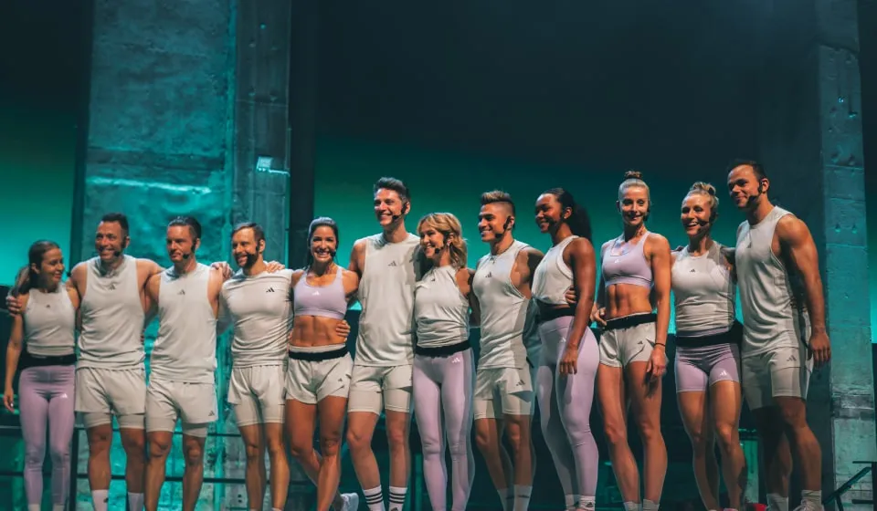 Group of Les Mills Core instructors dressed in adidas workout gear posing after working out on a stage