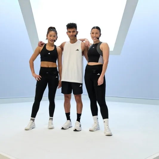 Three individuals wearing athletic clothing stand together in a well-lit studio with a minimalist design, commonly used for Les Mills Grit sessions.