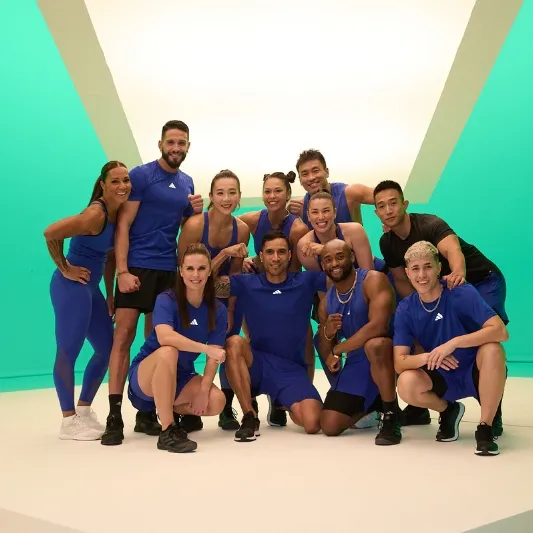 Nine people in blue athletic clothing posing in front of a green and white background, embodying their Les Mills BodyCombat spirit.