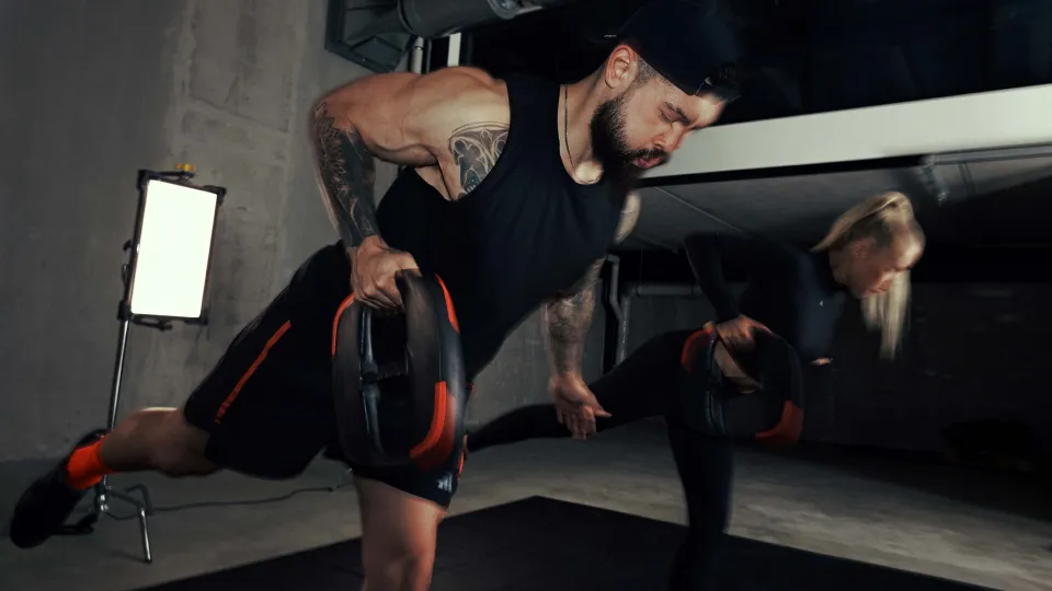 Two instructors each standing on one leg with a weight plate in their hands