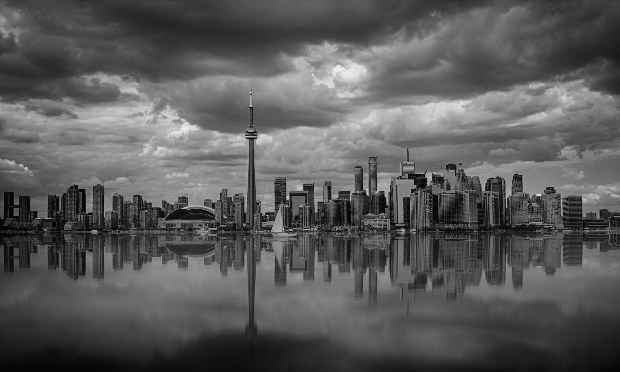 Toronto skyline at sunset, featuring the CN Tower and city buildings reflected in calm water. 