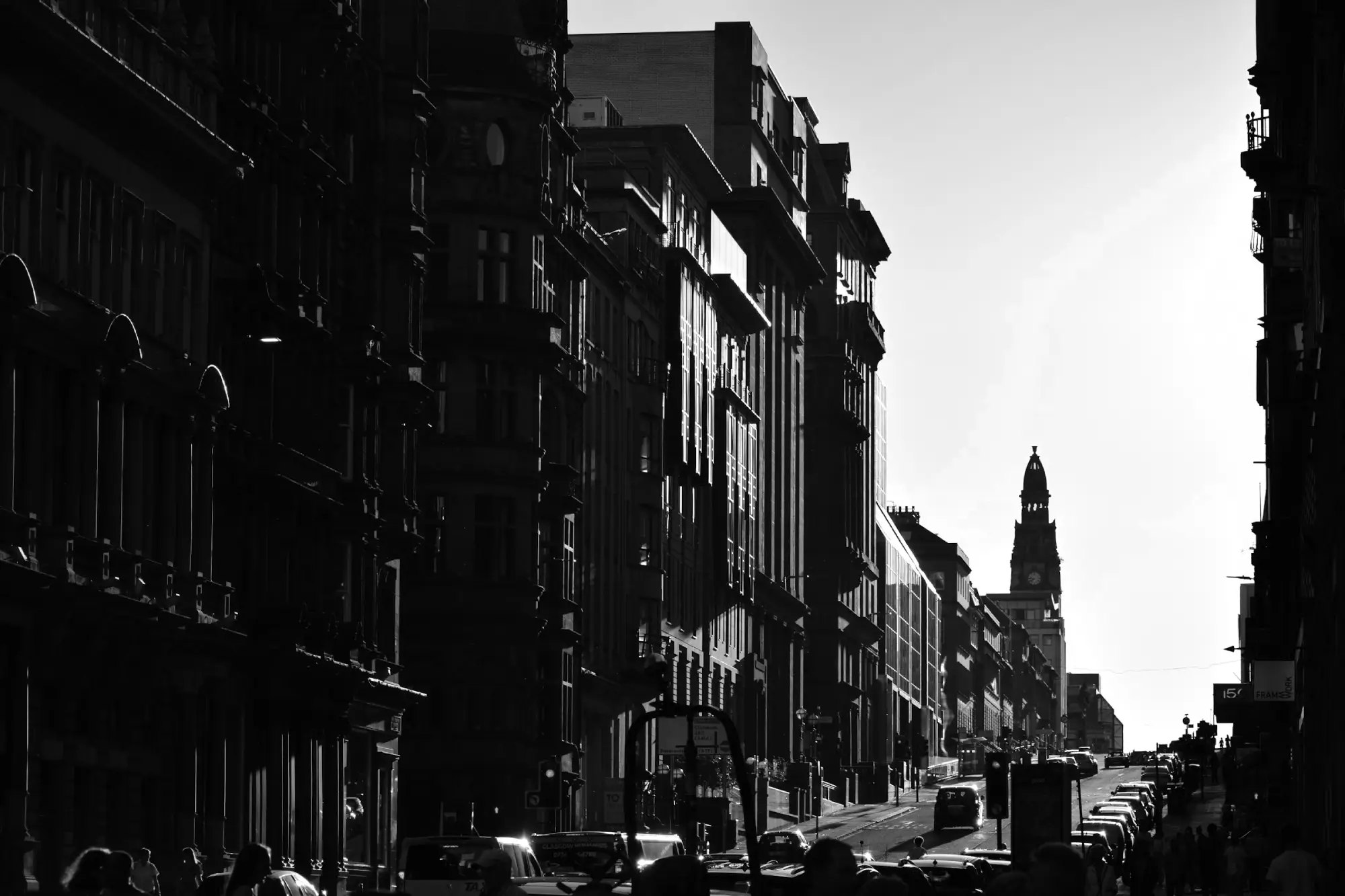 Street view of Glasgow, UK, showing a modern buildings lining a busy urban road, with a prominent clock tower or spire visible in the distance.