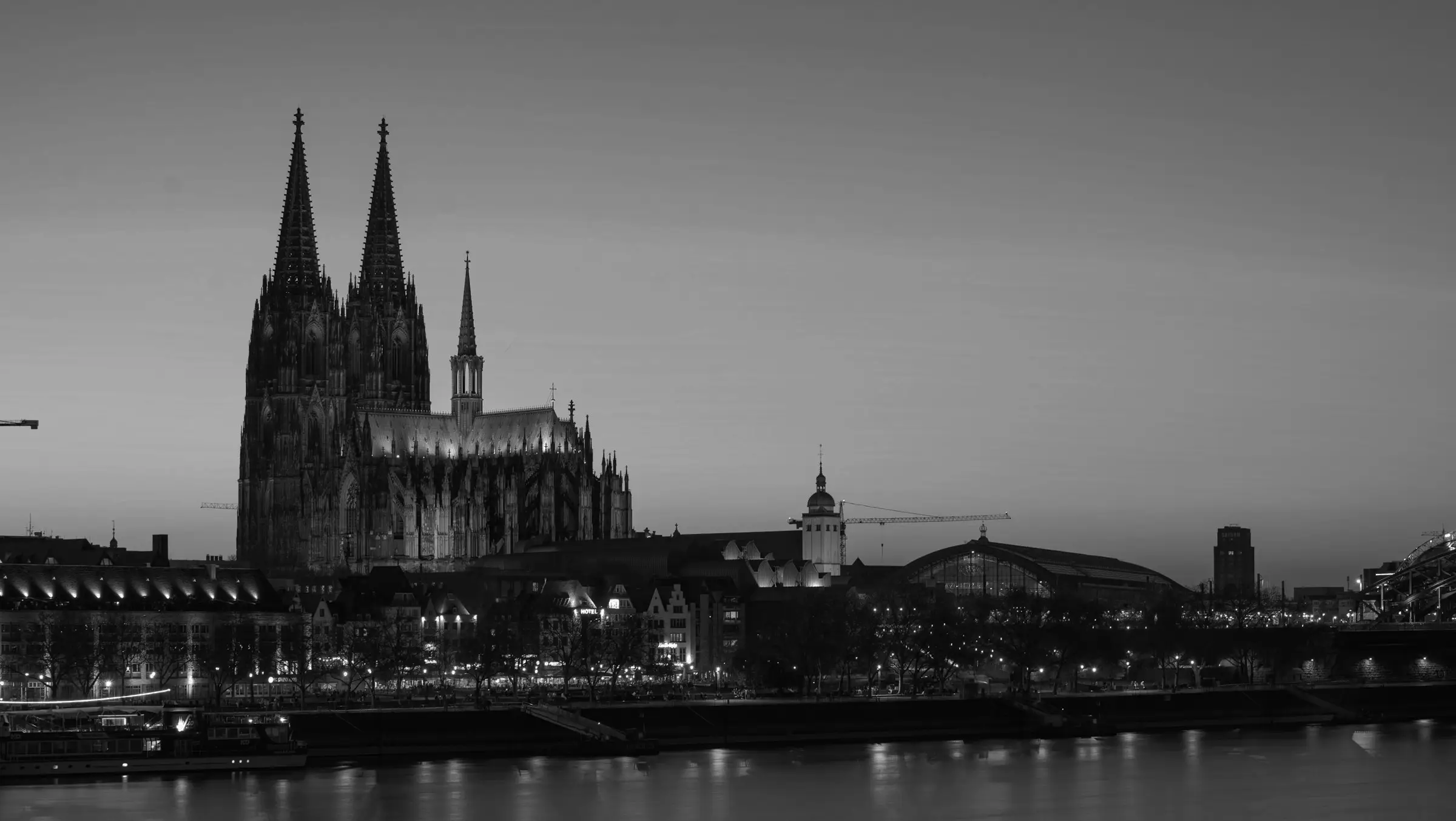 Illuminated riverfront view of Cologne featuring the twin-spired Cologne Cathedral