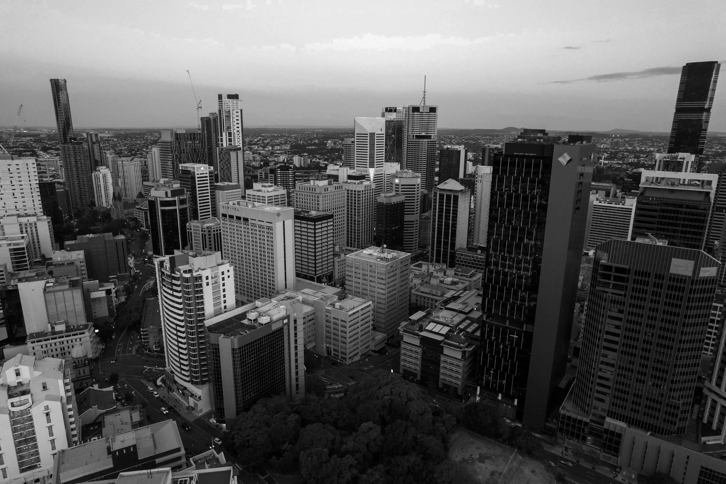 Aerial view of Brisbane CBD with high-rise buildings, cranes, and green space