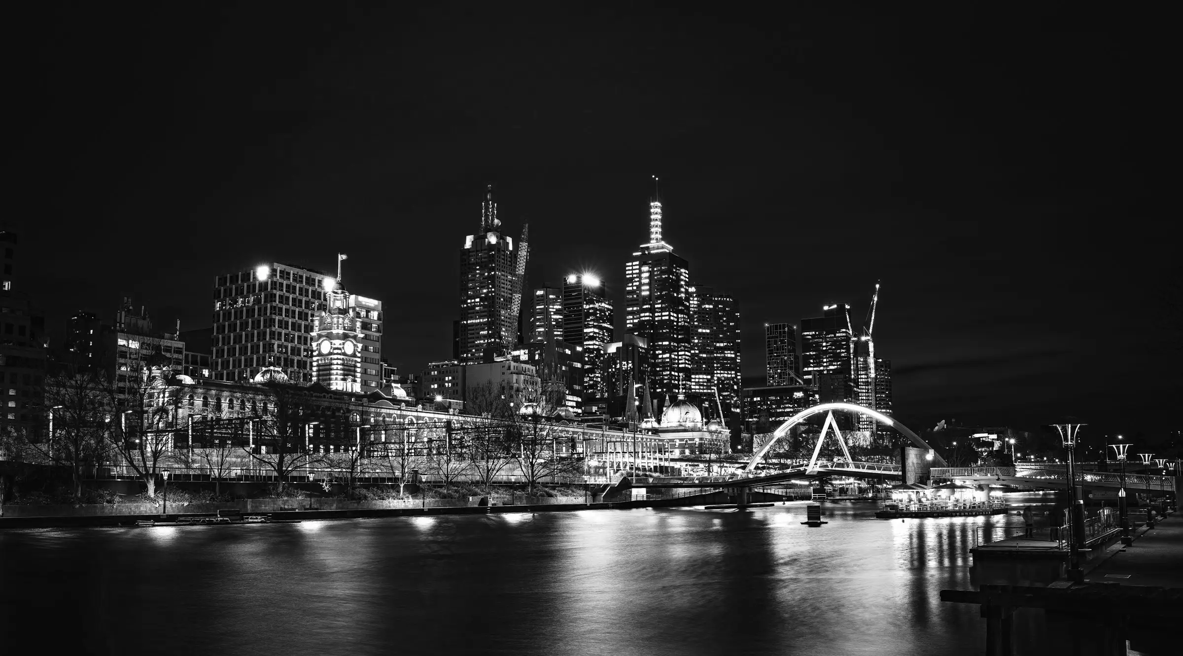 Night view of Melbourne skyline with illuminated buildings, Yarra River, and arched bridge