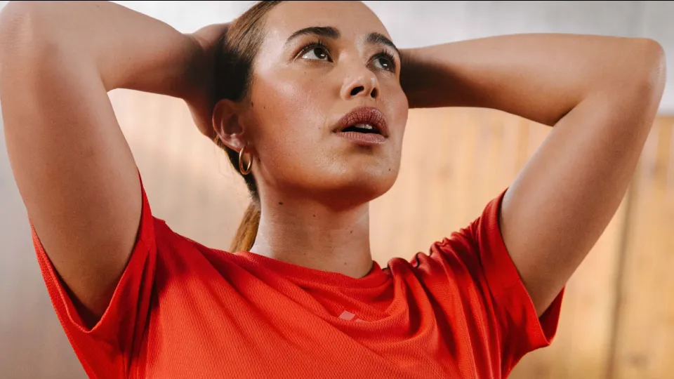 Person in a red shirt with hands behind head indoors