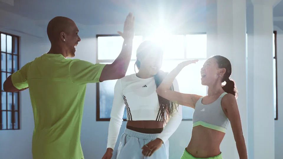 three people high-fiving indoors with sunlight streaming through large windows
