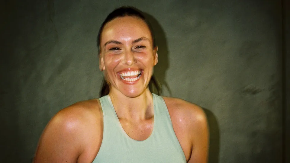 A person with a big smile wearing a light green athletic tank top