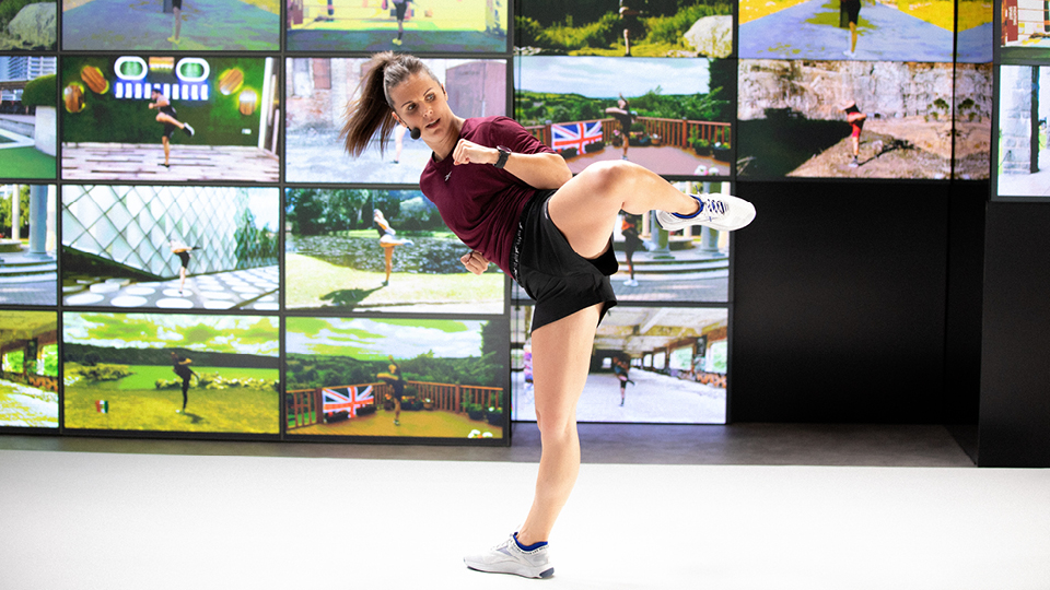 a woman performing high side kick in front of a wall of scenic screens
