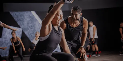 黒いスポーツウェアを着た複数人がジムでトレーニング。前景に2人が運動器具を使用。