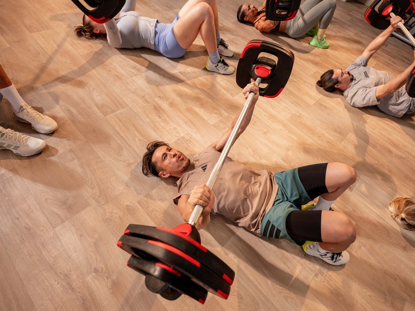 Close-up of two people lifting heavy barbells during a strength training class, showcasing effort and community support.