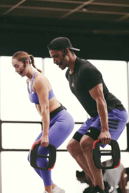 Two people lifting weight plates in a bent-over position during a strength training session in a bright studio.