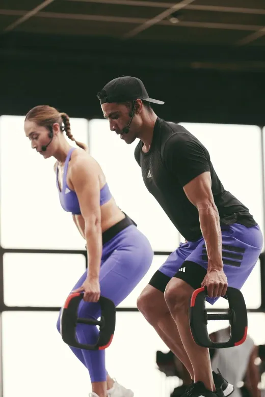 Two people lifting weight plates in a bent-over position during a strength training session in a bright studio.