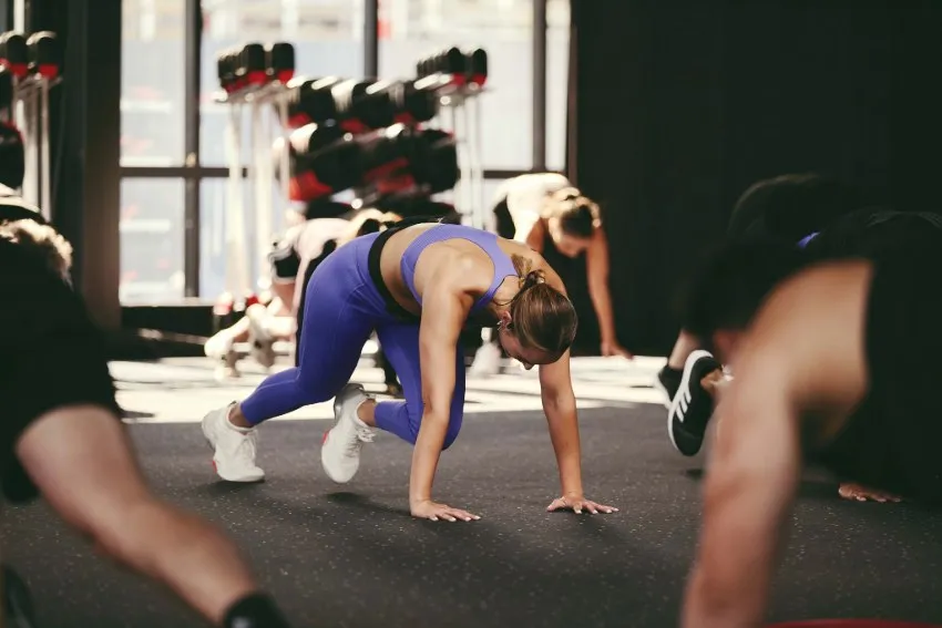 Group fitness class with six people performing floor exercises in a bright studio, focusing on strength and mobility.