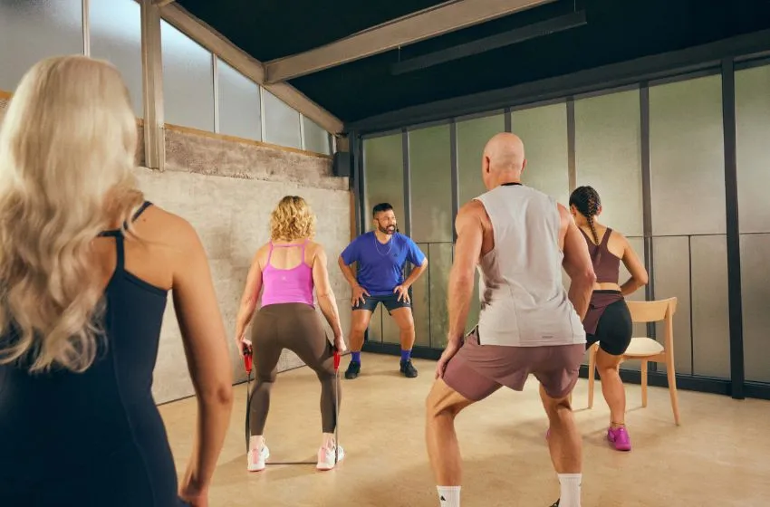 Group of five adults exercising indoors with resistance bands while a male instructor leads the workout.